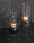 Two glass candle holders with candles on a dark background