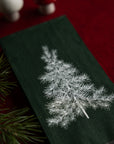 Green fabric with embroidered white pine tree design on a red background