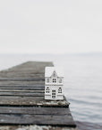 Small white house model on a wooden pier extending into a body of water with a foggy background.
