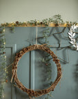 Decorative wreath with pinecones and greenery on a teal wall with a gold candle holder and star decorations.