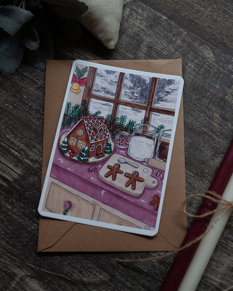 Greeting card with a gingerbread house design on a wooden surface with a candle.