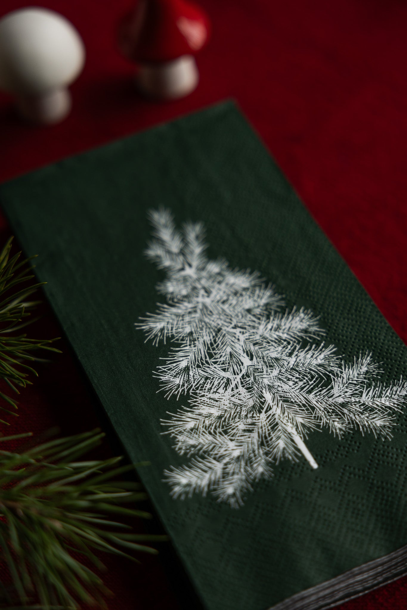 Green fabric with embroidered white pine tree design on a red background