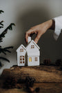 Hand placing two small white house-shaped lights on a wooden surface with a blurred background
