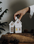 Hand placing two small white house-shaped lights on a wooden surface with a blurred background