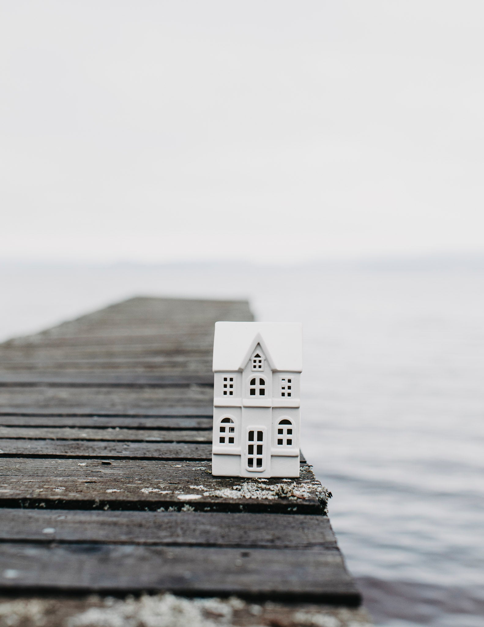 Small white house model on a wooden pier extending into a body of water with a foggy background.