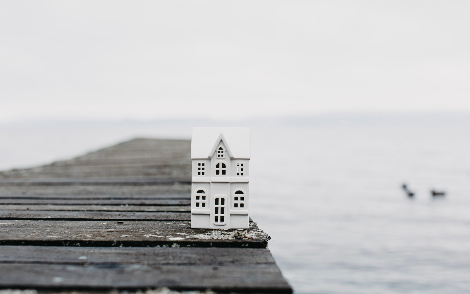 Small model house on a wooden pier extending into a body of water.