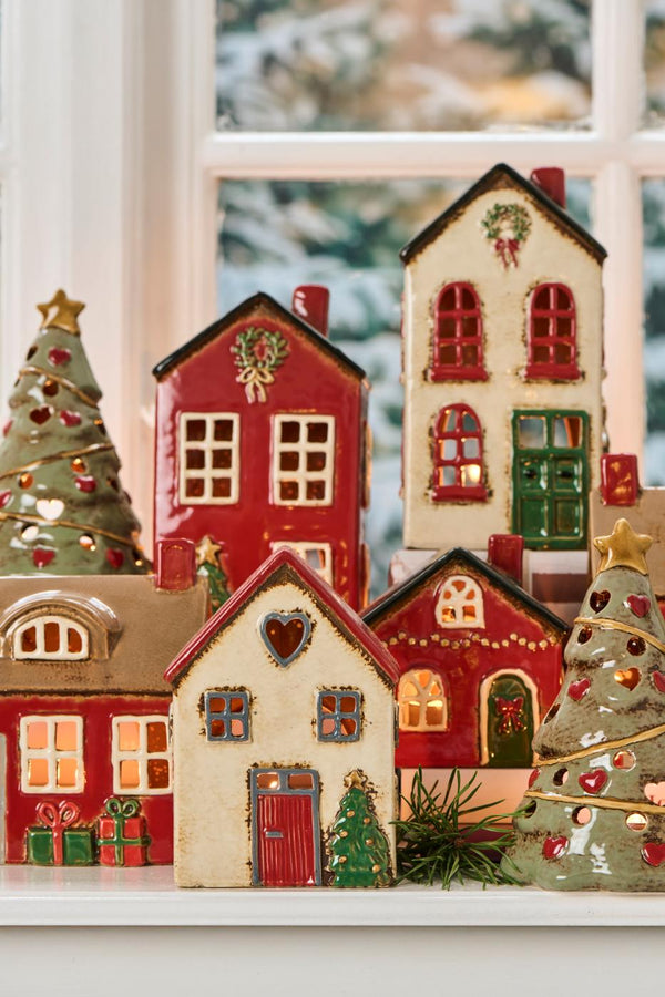 Decorative ceramic houses and trees on a windowsill with a snowy outdoor background.